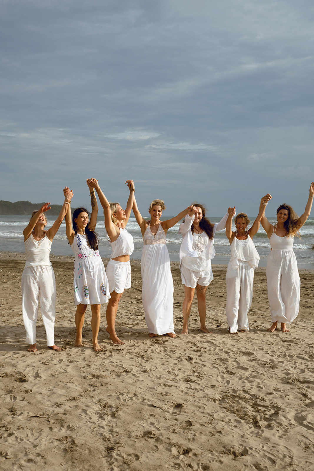 Frauen in weißen Kleidern halten Händchen am Strand und feiern gemeinsam